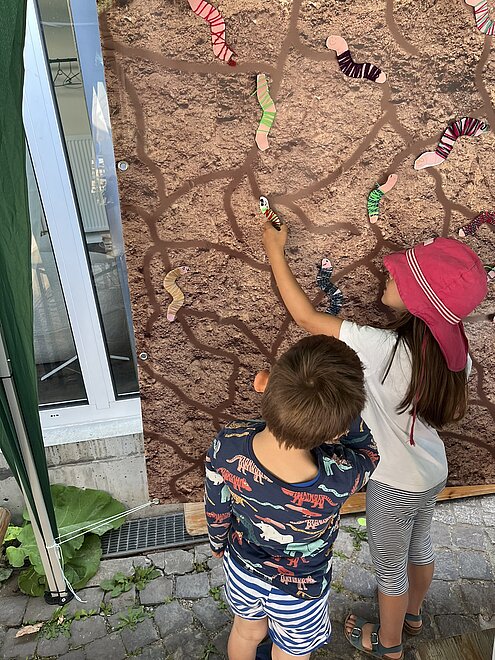 Kinder kleben gebastelte Regenwürmer an die Wand.
