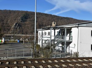 Übersichtsfoto der Lärmmesstation in Assmanshausen. Es sind die Schienen zu sehen, sowie das Haus der Vereine an dem die Messeinrichtungen angebracht sind. in Hintergrund ist der Rhein zu sehen.