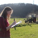 Eine Gutachterin notiert im Gelände Daten zu einer landwirtschaftlich genutzten Stichprobenfläche