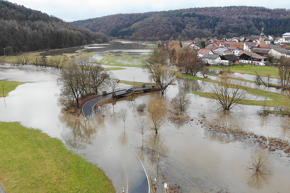 Grüne Wiesen und eine Straße, die von braunem Wasser großflächig bedeckt sind
