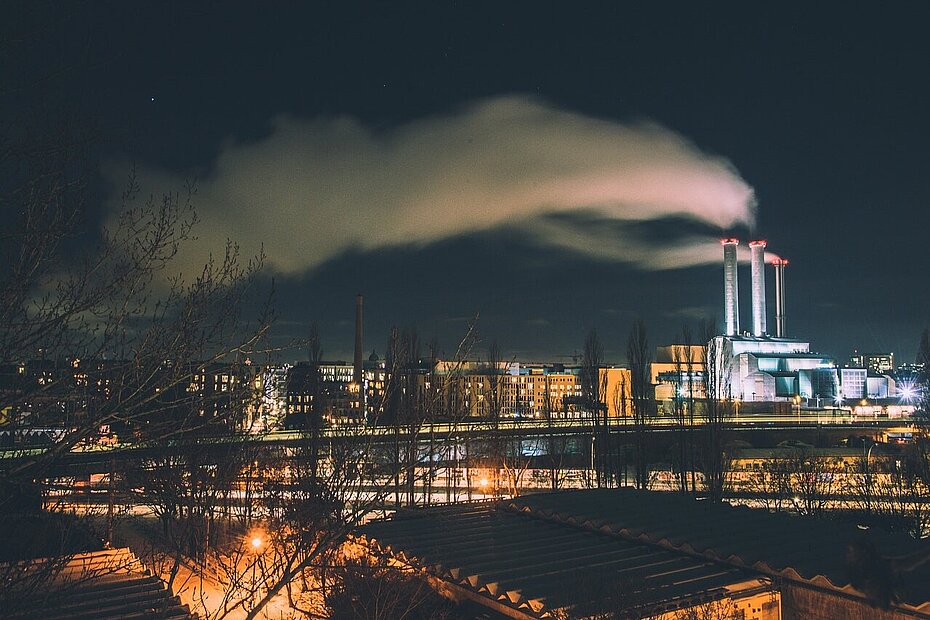 Stadt in der Nacht mit rauchenden Fabrikschornsteinen