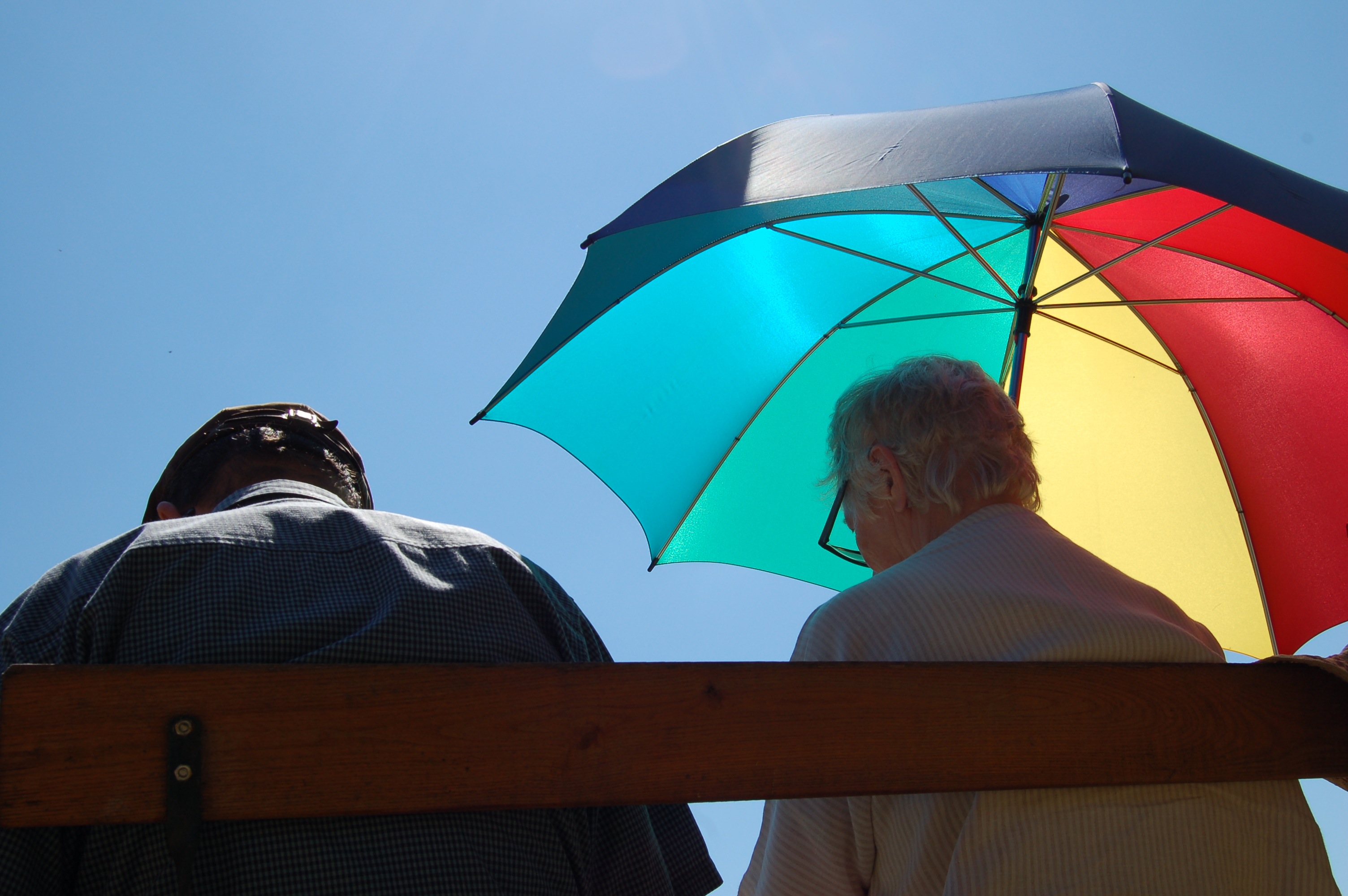 Menschen sitzen mit Regenschirm als Hitzeschutz auf einer Bank